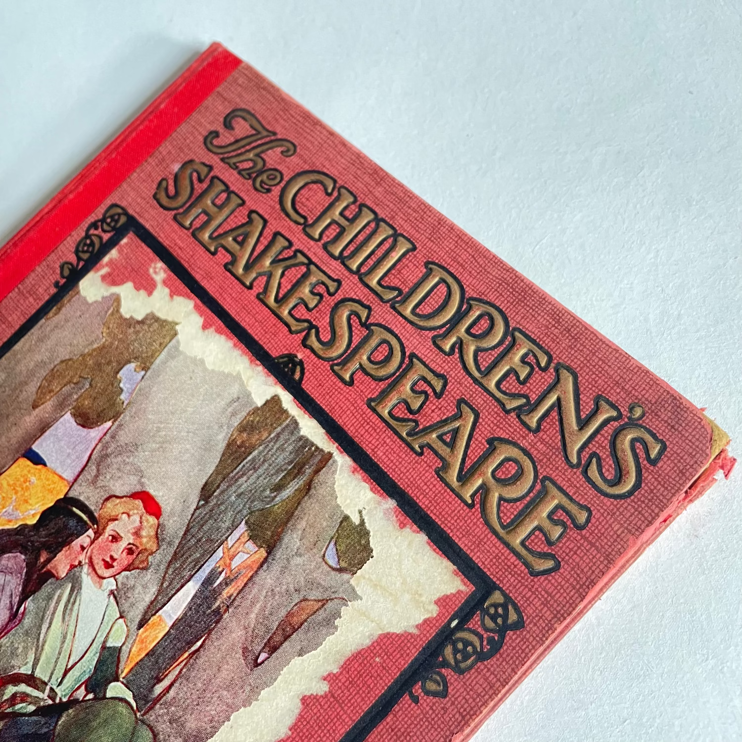 Vintage book titled 'The Children's Shakespeare' with red cover and illustrations on a light blue background