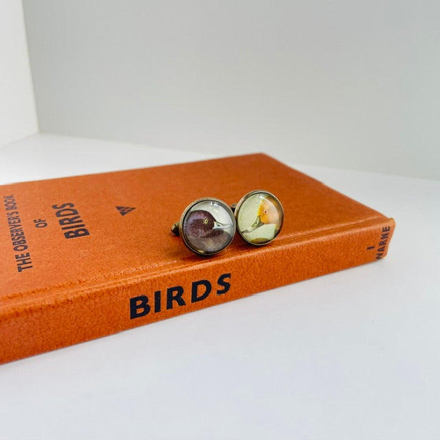 Cufflinks with bird designs on a book titled 'The Observer's Book of Birds' on a white surface.