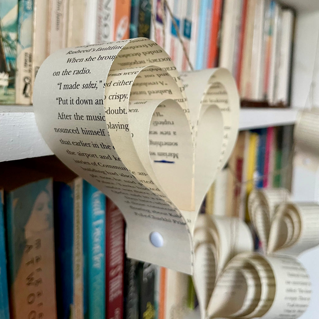 Heart-shaped ornament made from  book pages on a bookshelf with books in the background