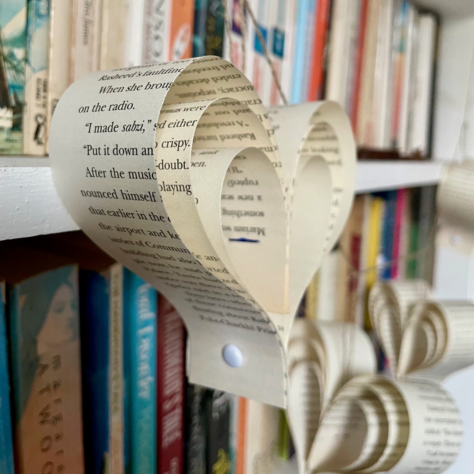 Heart-shaped ornament made from  book pages on a bookshelf with books in the background