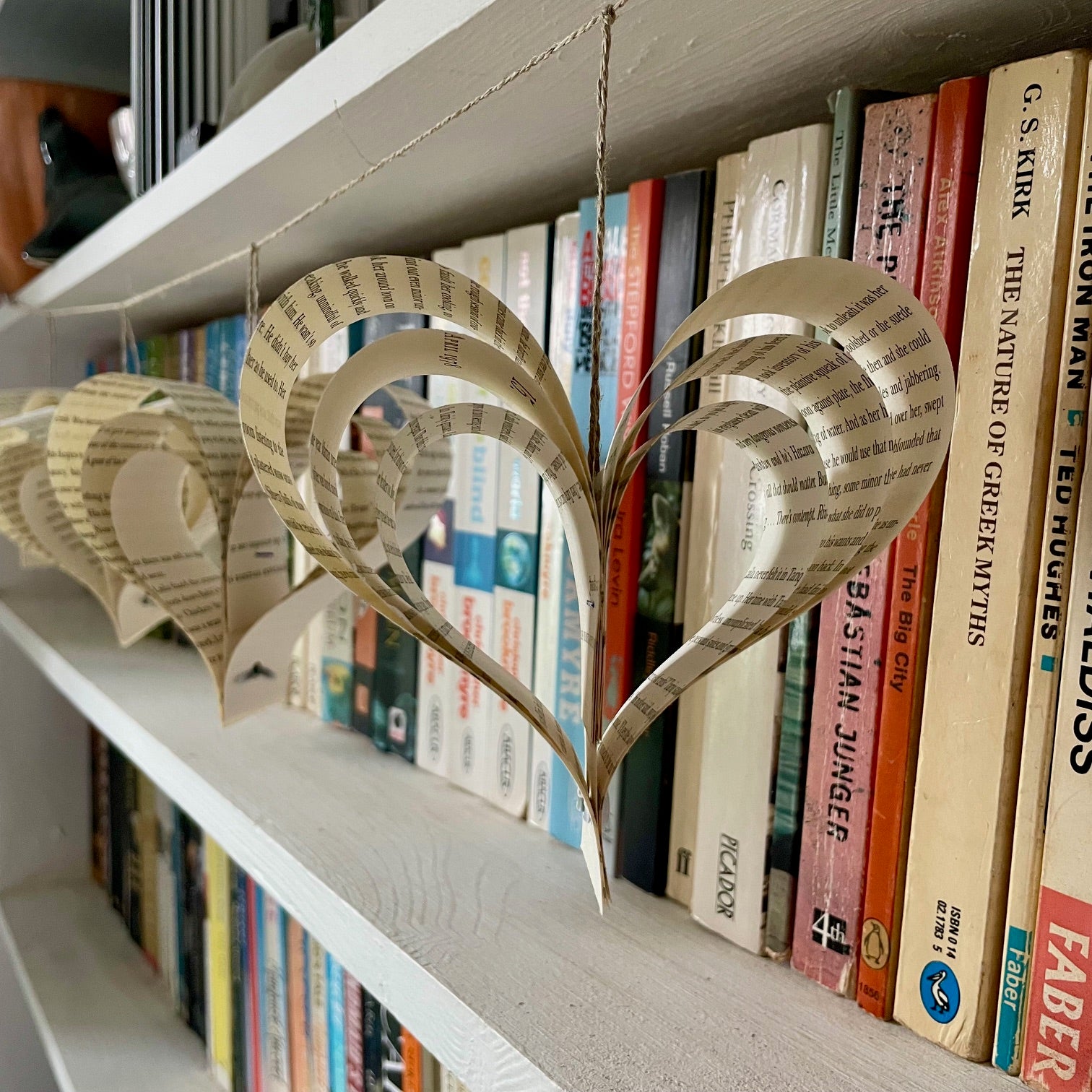 Heart-shaped garland made from paper on a bookshelf with books in the background.