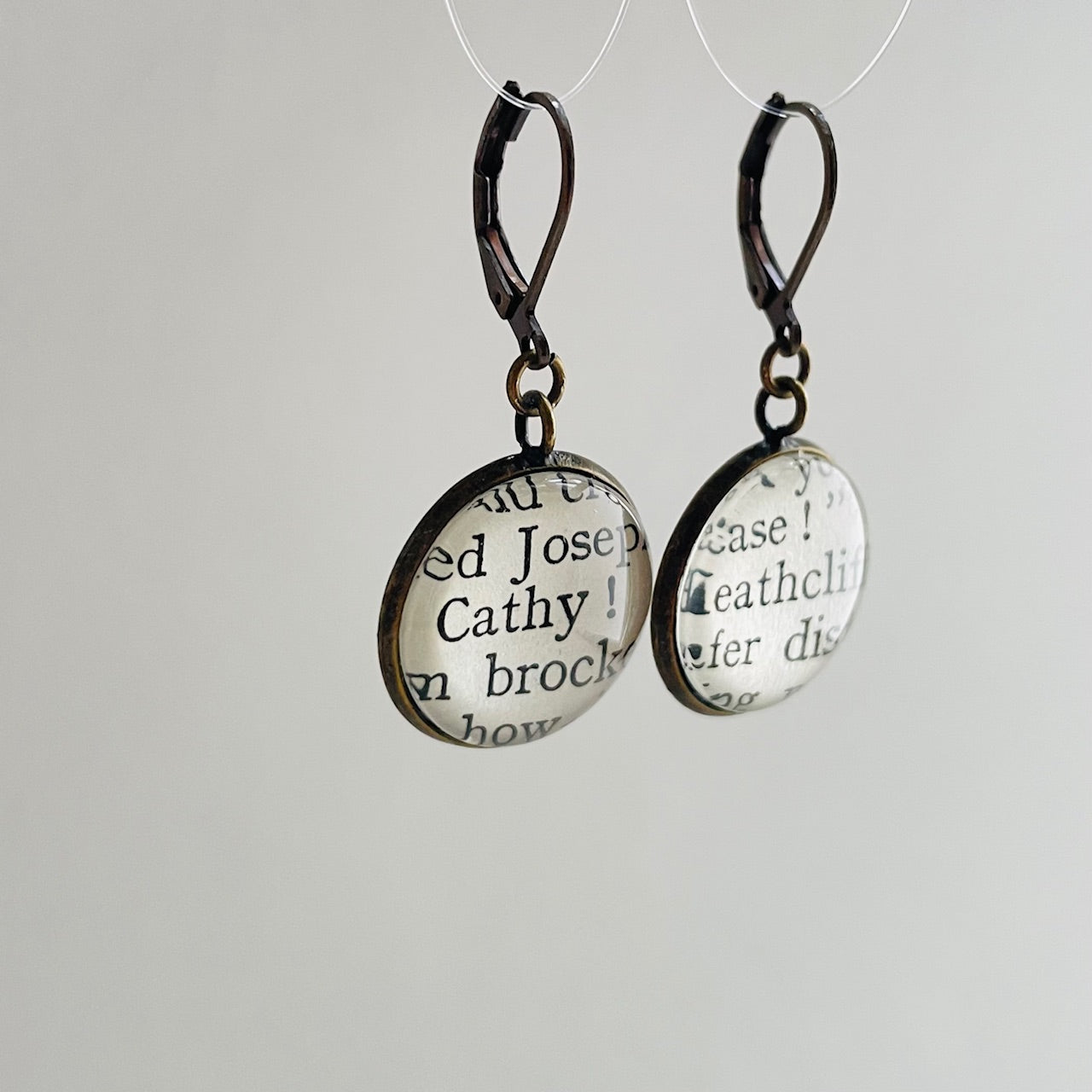 a pair of round bronze dangle earrings with 'Heathcliff' and 'Cathy' taken from real book pages. 