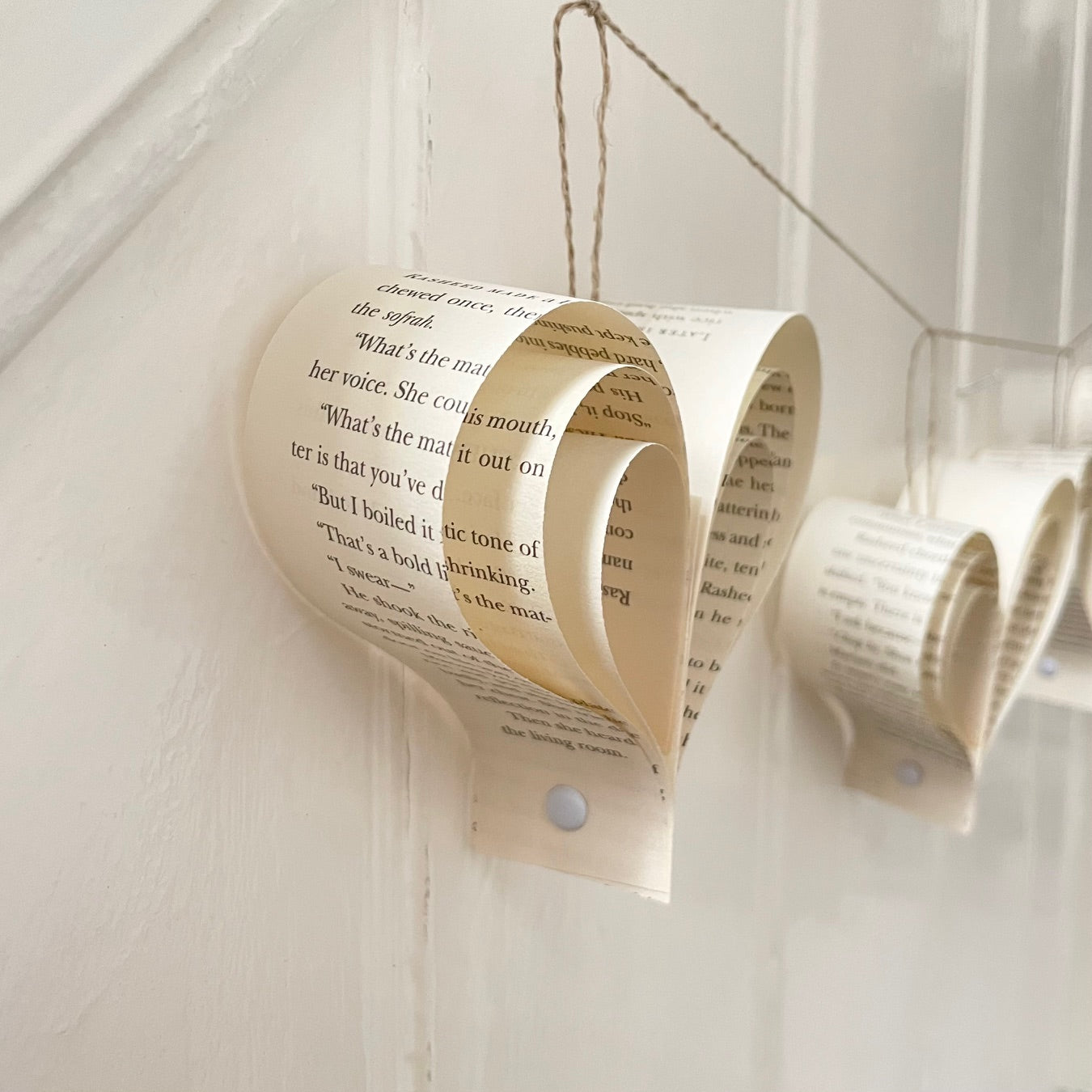 Decorative wall art made from rolled-up paper with text, hanging against a white wooden panel background.