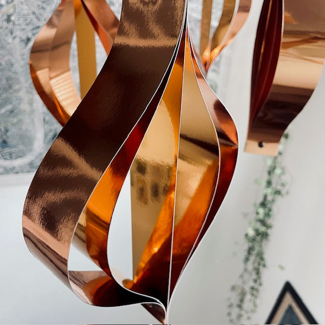 Copper-colored metal sculpture with wavy design on a white surface