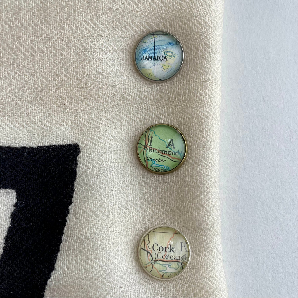 three small round glass and metal brooches or pins customised with paper maps