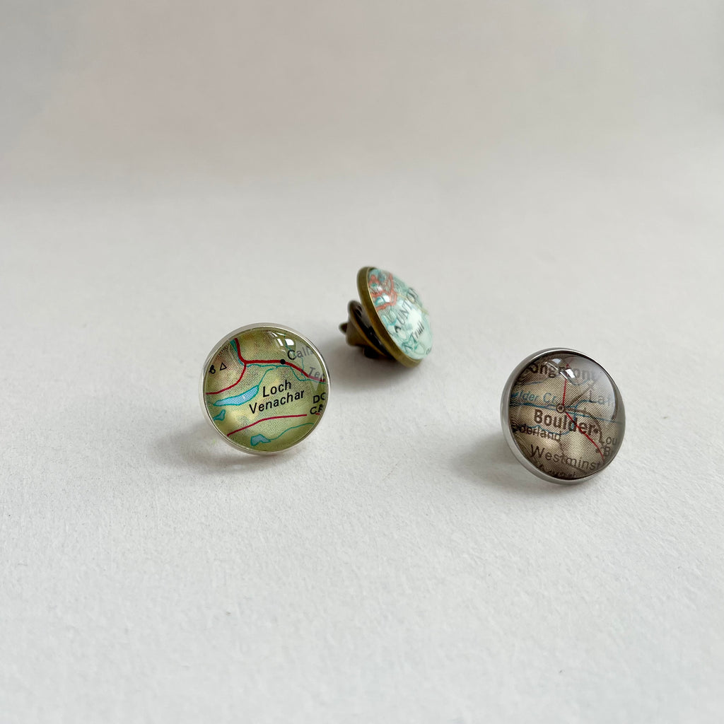 three small round glass and metal brooches or pins customised with paper maps