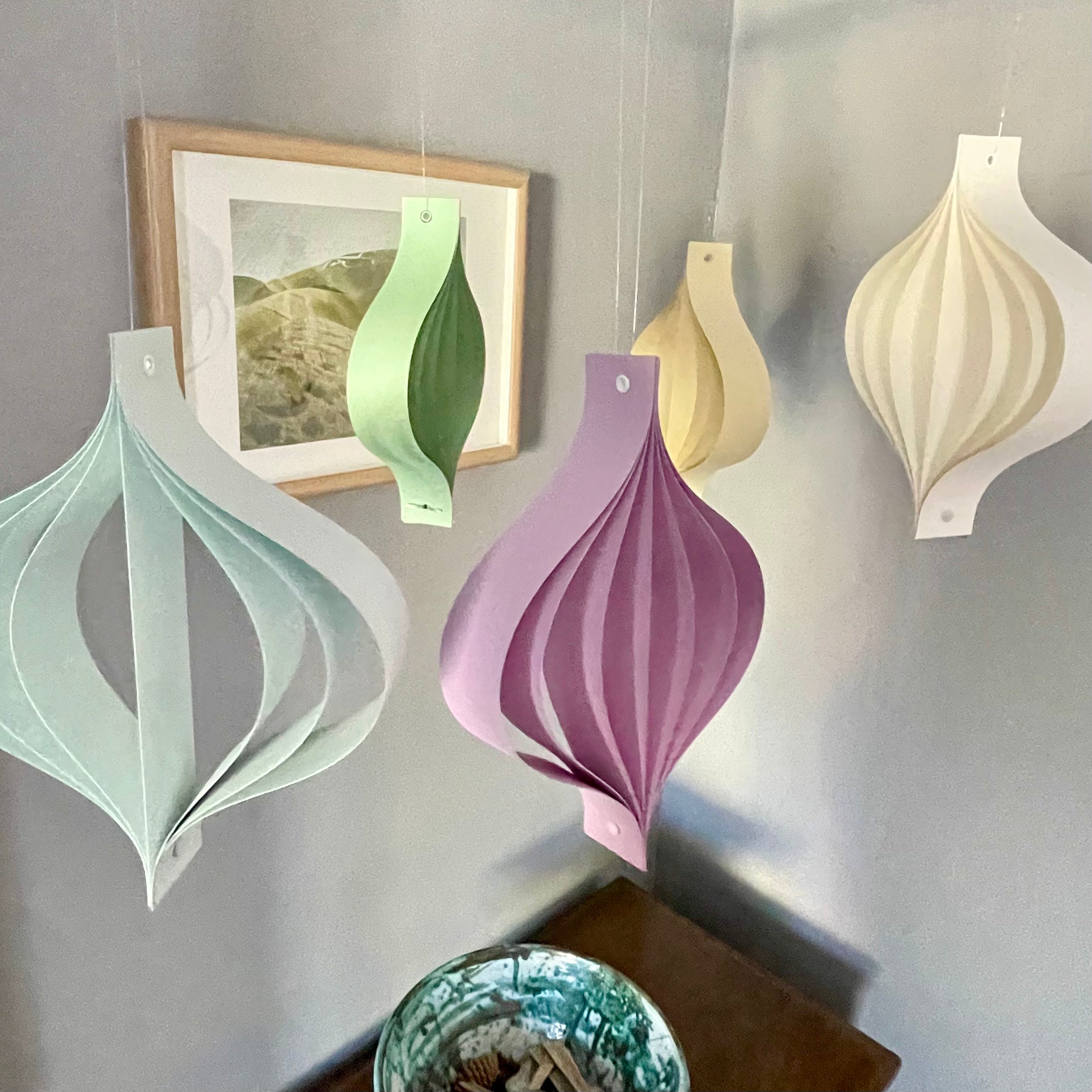 Decorative paper lanterns hanging on a wall with a framed picture in the background.