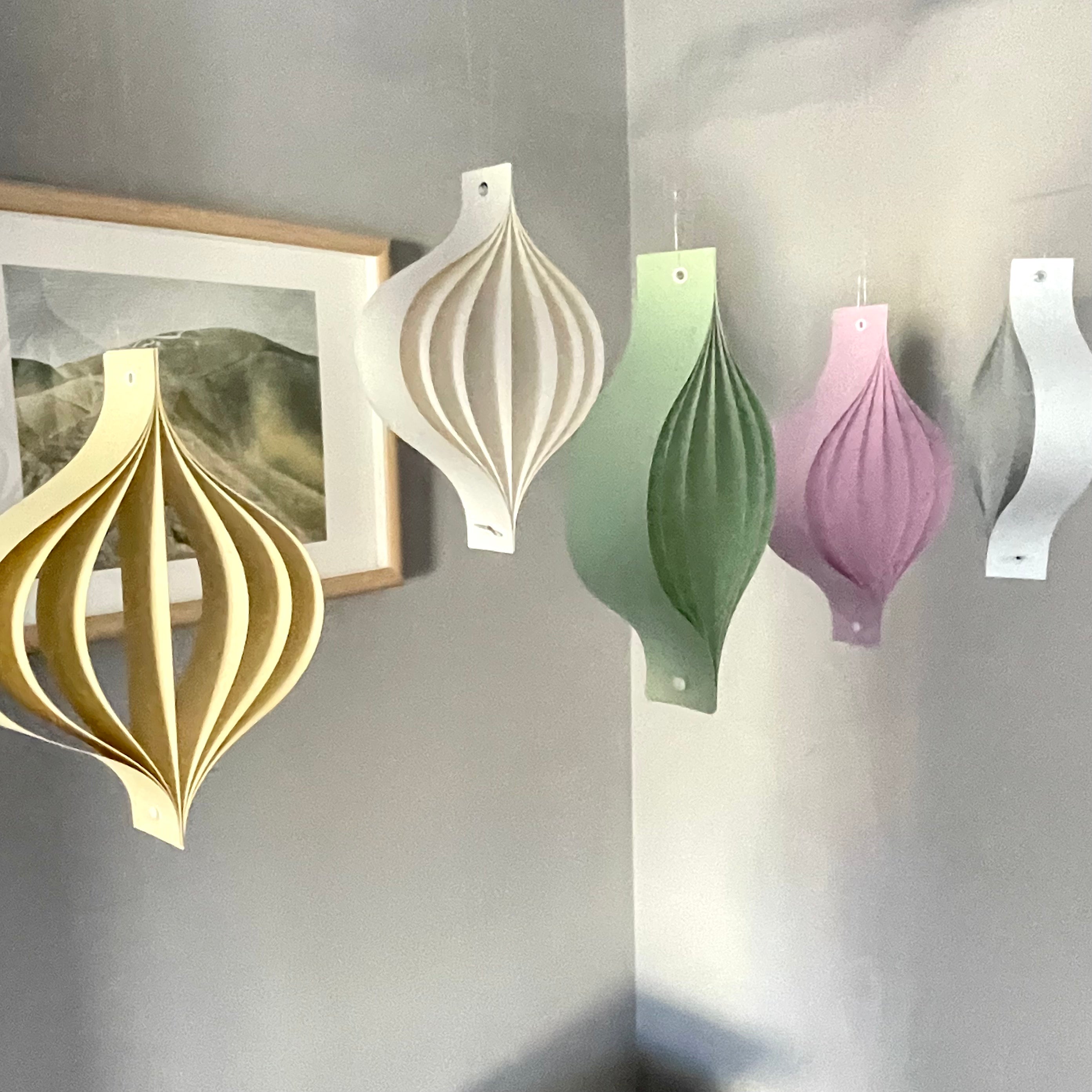 Decorative pastel hanging ornaments in various colors on a gray wall.