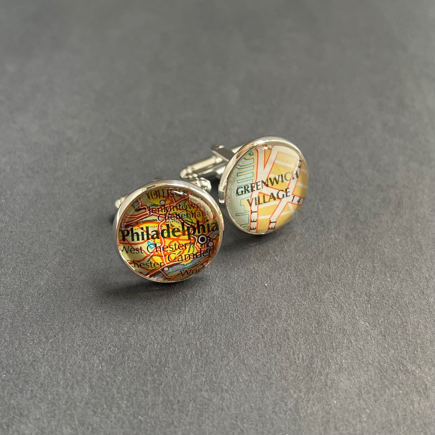 round silver cufflinks set with map roundels covered in a dome of clear glass. the cufflinks show the city of Philadelphia and the locale of Greenwich Village in New York