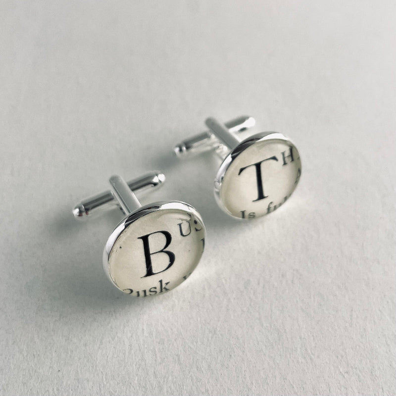 Pair of silver personalised intial cufflinks with letter 'B' and 'I' on a light gray background. 